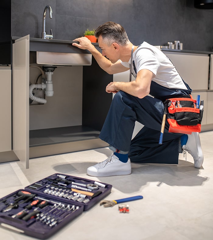 Plumber inspecting sink plumbing with tools on floor.